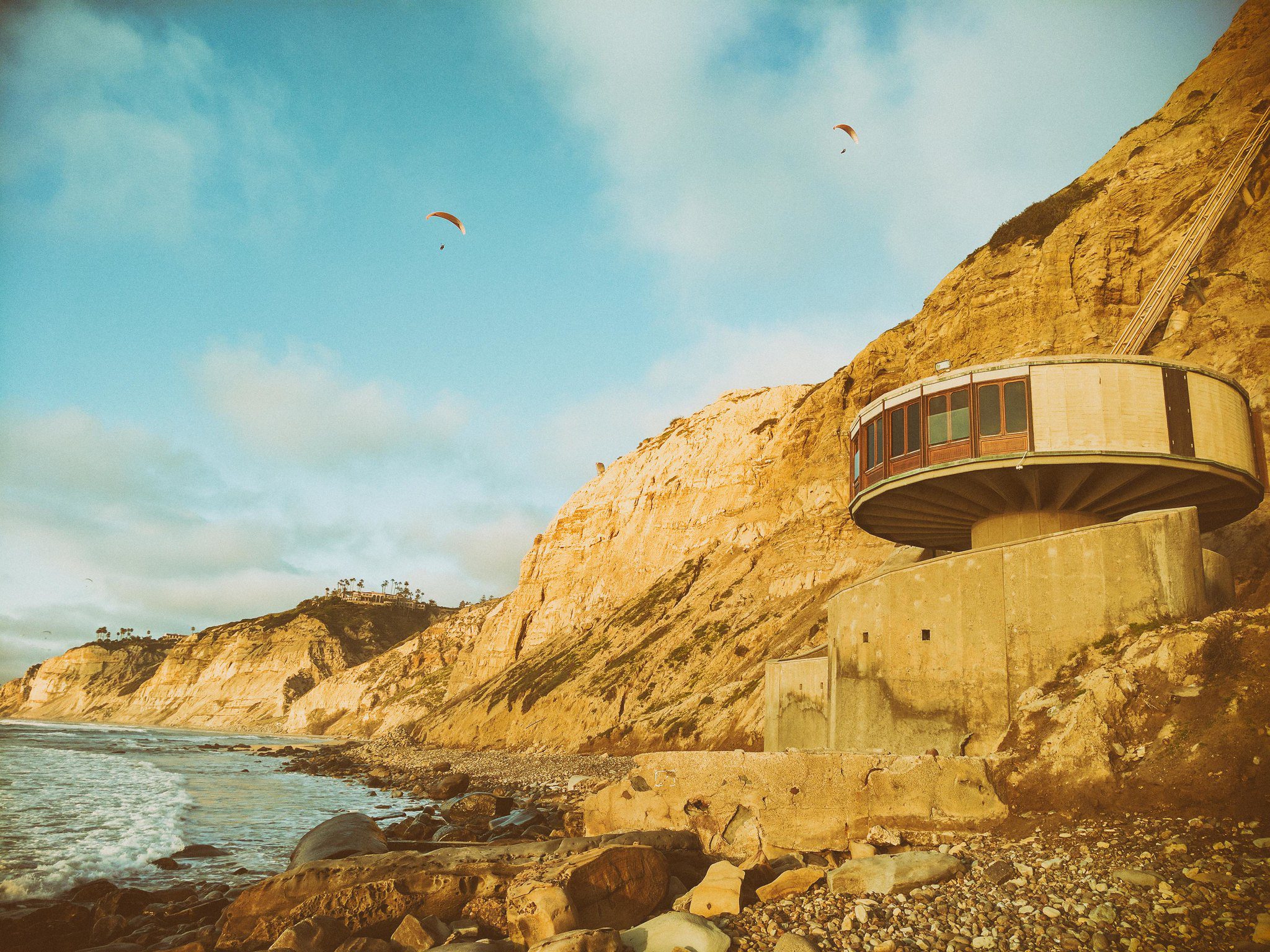 The round mushroom house in La Jolla sits hidden below towering cliffs at Black's Beach with paragliders flying overhead