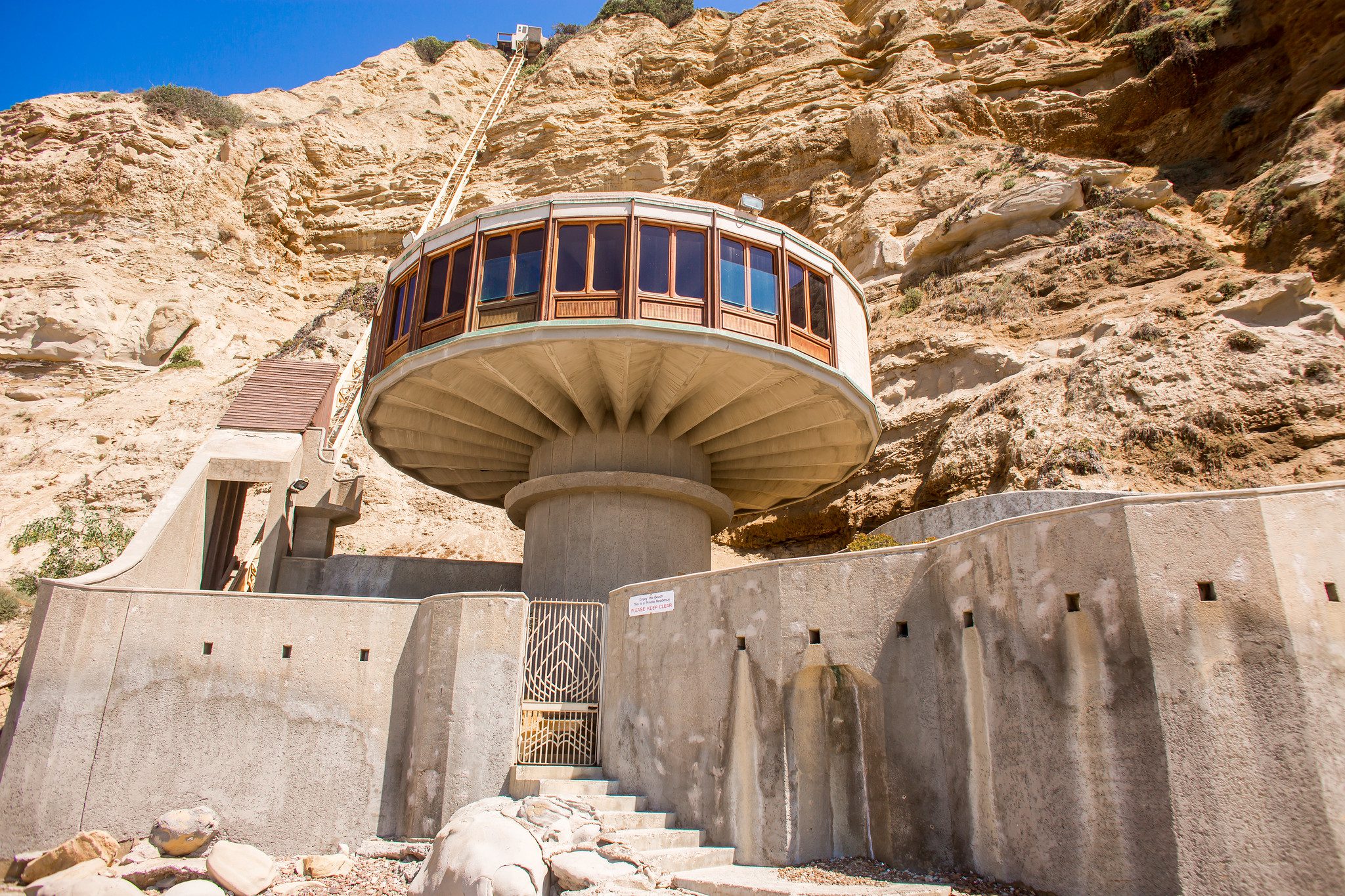front view of mushroom house circular concrete structure surrounded by concrete walls and 300 foot tram going up the cliff