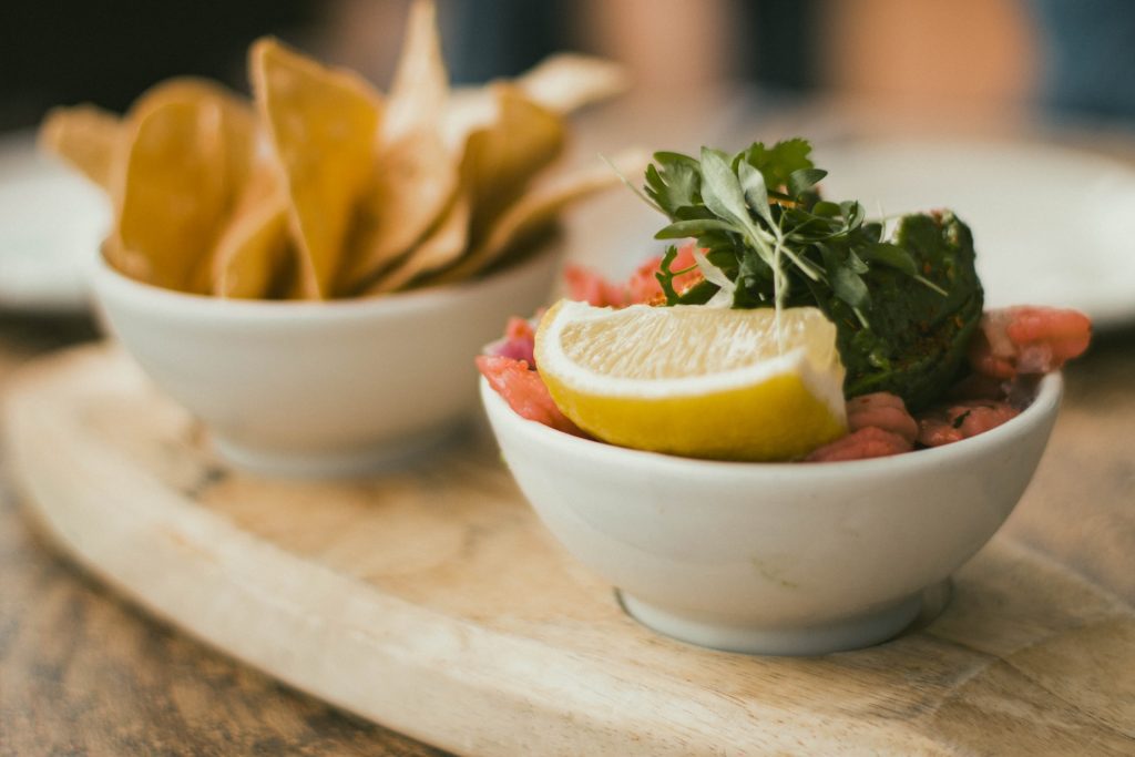 two small white bowls holding tortilla chips and ceviche with cilantro and a slice of lemon