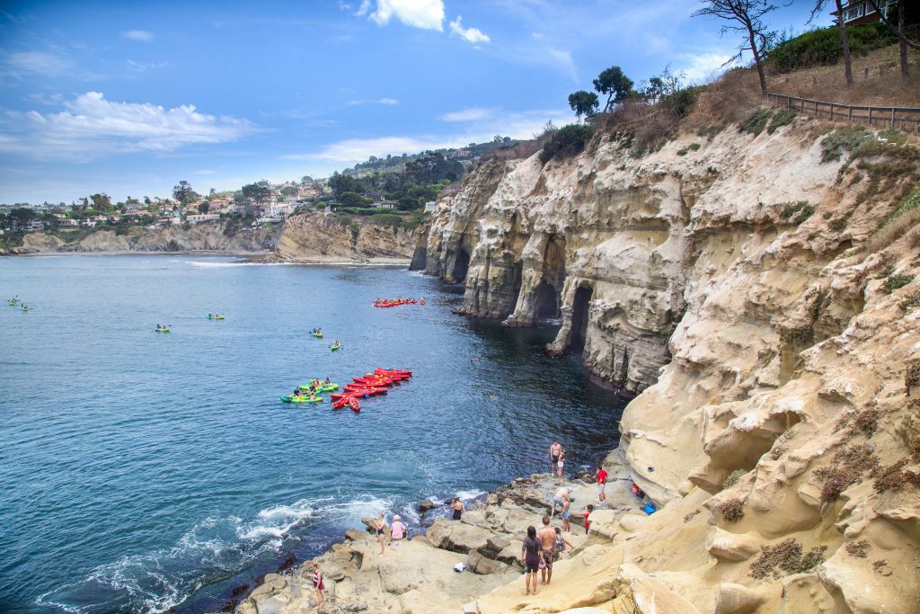 a group of kayakers explore the seven sea caves in La Jolla cove as people watch from the shore
