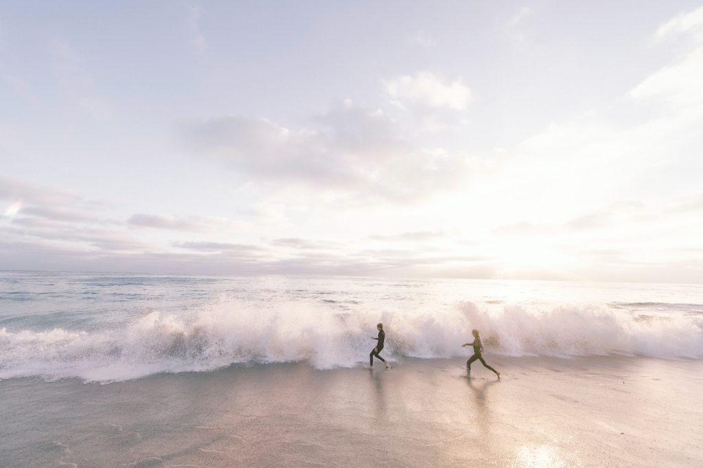 two people run across the sand into a breaking wave on La Jolla Shores beach, one of the top La Jolla beaches 