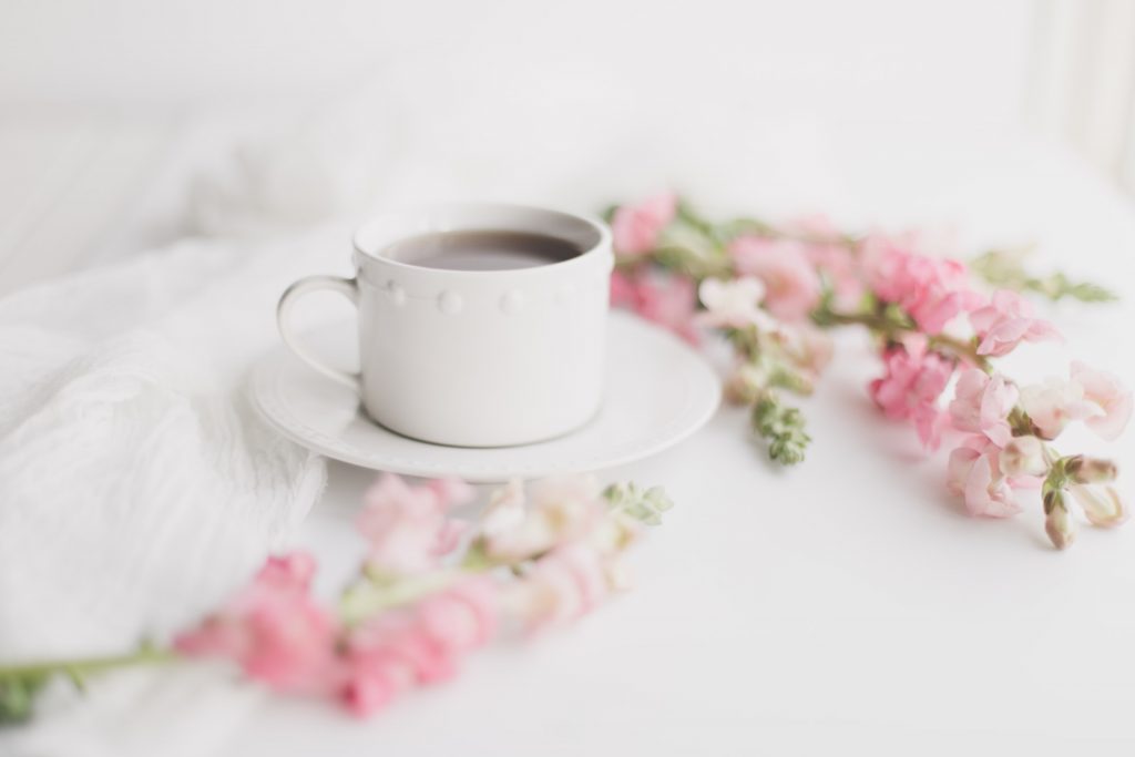 white tea cup and saucer on white table adorned with light pink flowers