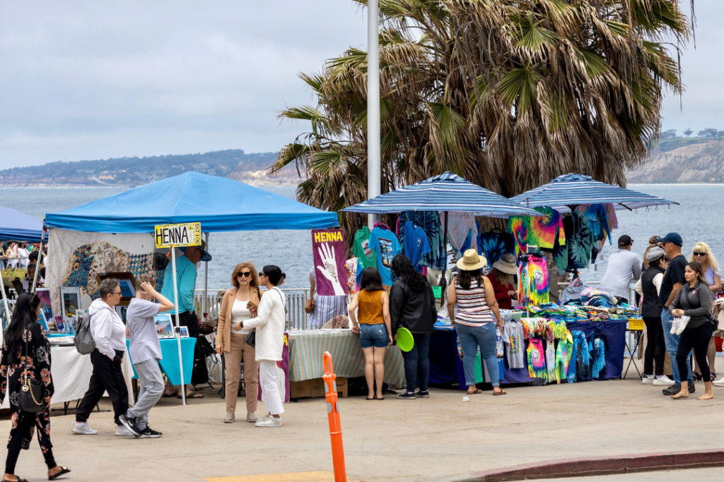 people walk by and shop from sidewalk vending booths in La Jolla cove