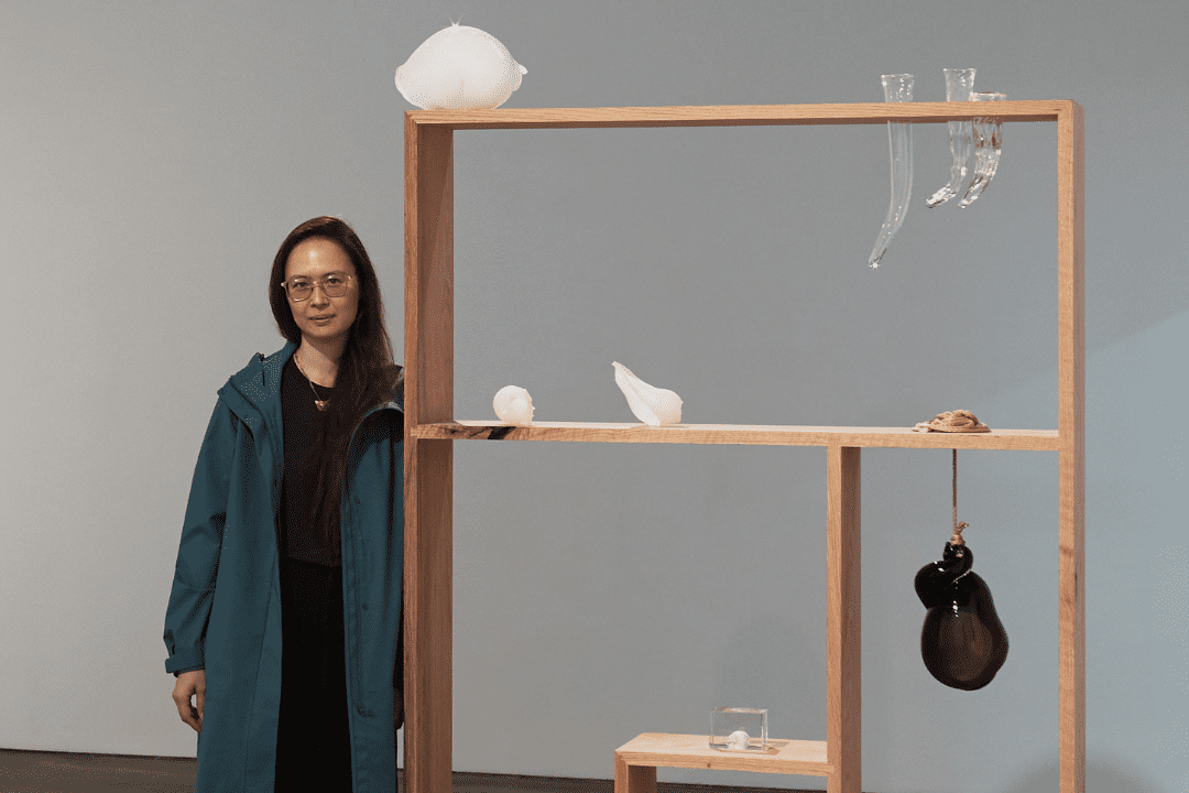artist Kelly Akashi stands next to blown glass creations displayed