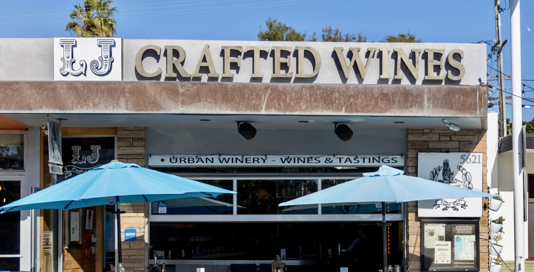 business front of LJ Crafted Wines with two blue umbrellas and patio seating