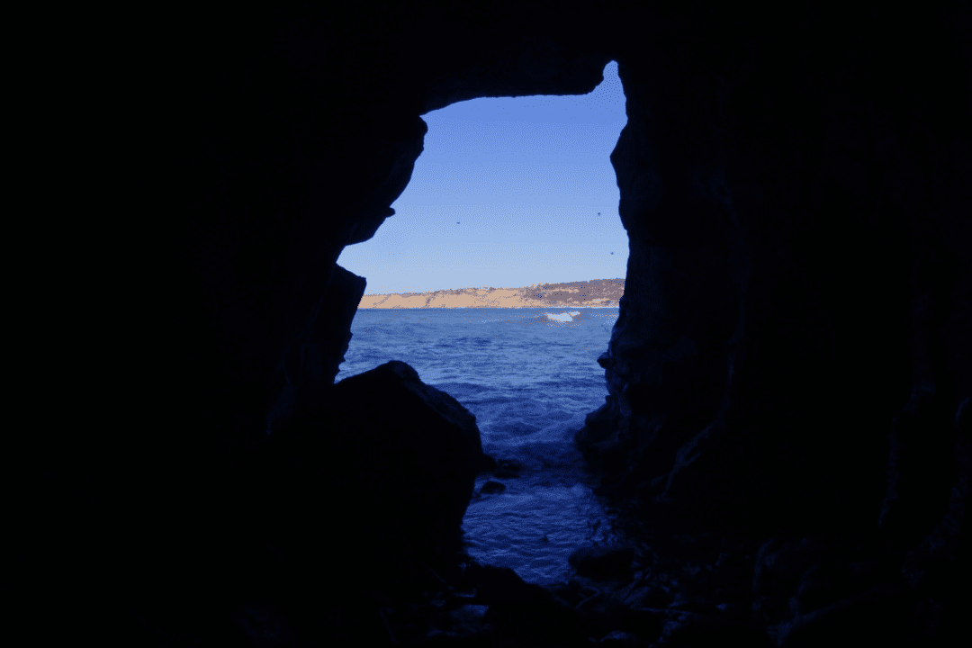 view from inside of sunny Jims sea cave provides a view of the La Jolla cove and Torrey Pines cliffs in the distance. silhouette of cave opening resembles a 1920s cartoon mascot for British Force Wheat Cereal.