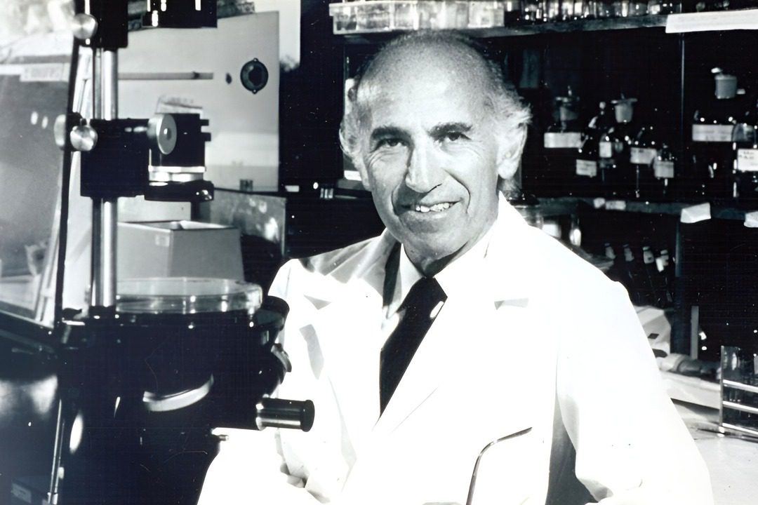 jonas salk sits in his laboratory wearing white coat with lab machines around him