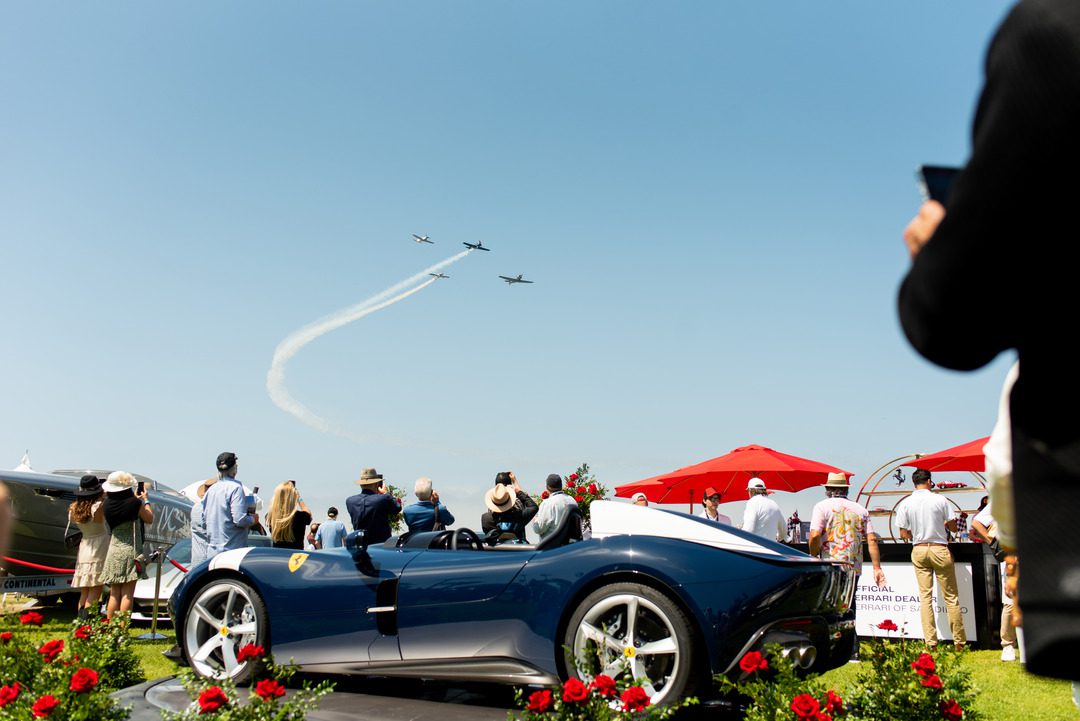four vintage planes fly over la jollas coast. a classic luxury car sits in the foreground while onlookers enjoy the flyover.