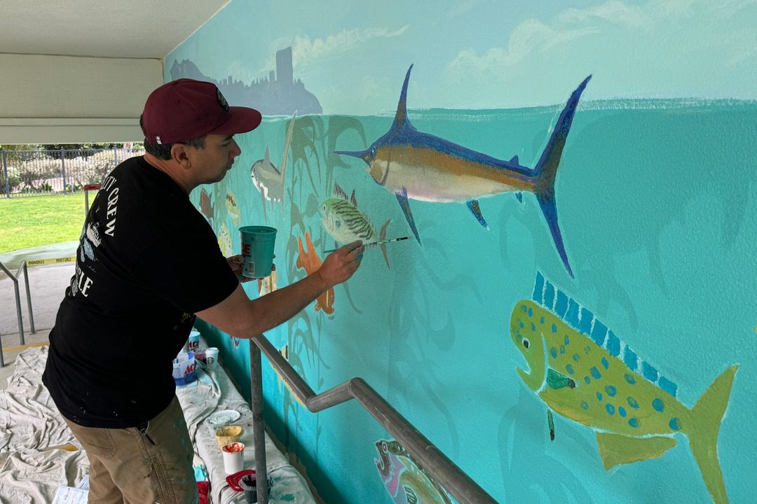 artist amadeo bachar painting a swordfish for underwater scene in mural at the children's school