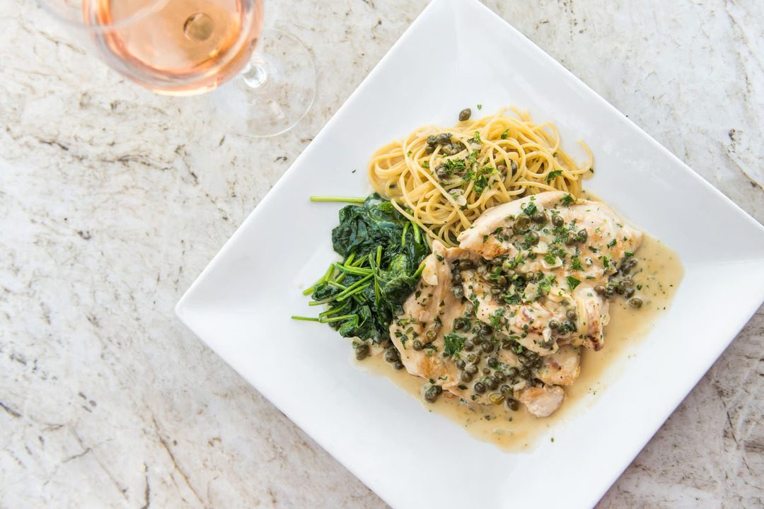 plate of noodles, spinach, and chicken topped with capers served on a white plate at one of the many italian restaurants in la jolla.