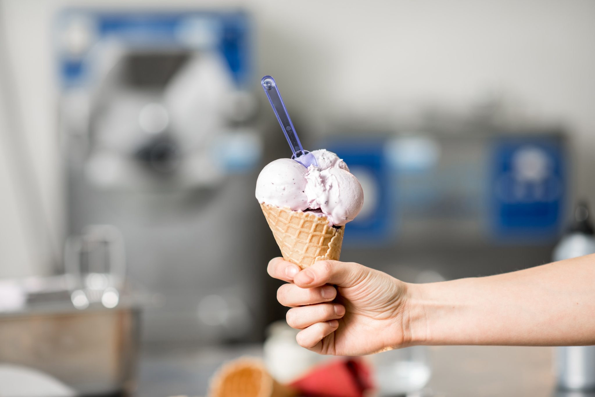 Holding waffle cone with ice cream at the kitchen with food ingredients and ice cream maker machine on the background