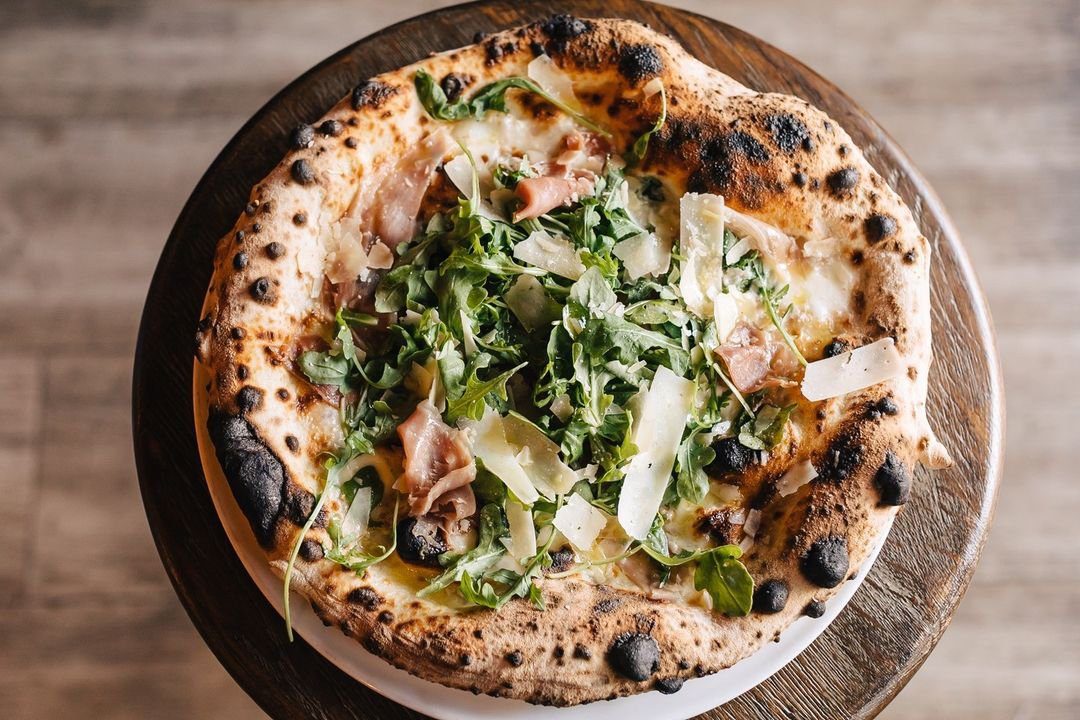 woodfired pizza with arugula and shaved parmesan cheese on top served at one of the many italian restaurants in la jolla.