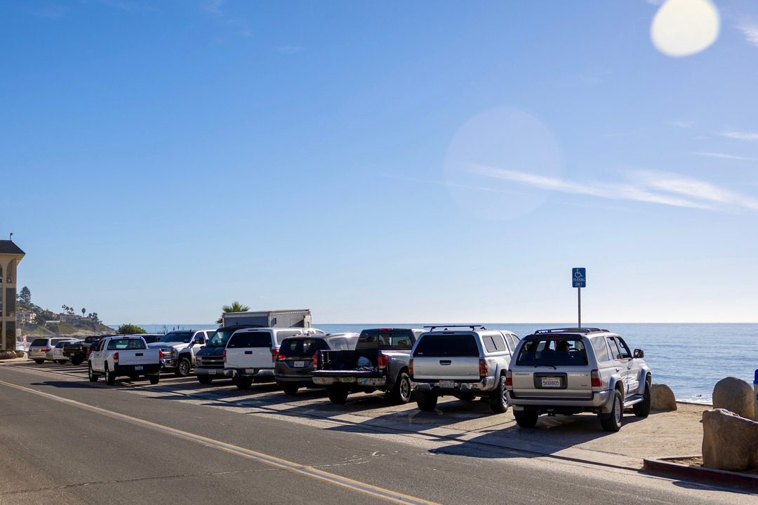 La Jolla parking area by the ocean, showing several cars parked along the street with a clear blue sky and a handicap parking sign, offering a scenic coastal view.