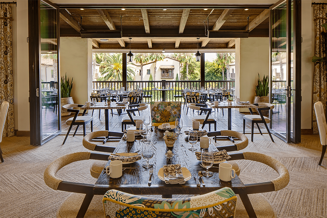 Elegant indoor-outdoor dining setup at Greenfinch Restaurant, located at Estancia La Jolla, with garden views and natural light.