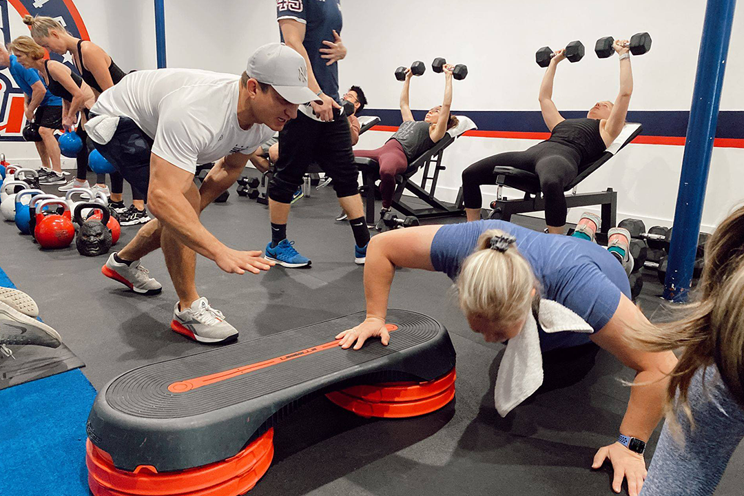 F45 gym in La Jolla showing group fitness class with personal trainer coaching members through functional workout using step platforms and dumbbells