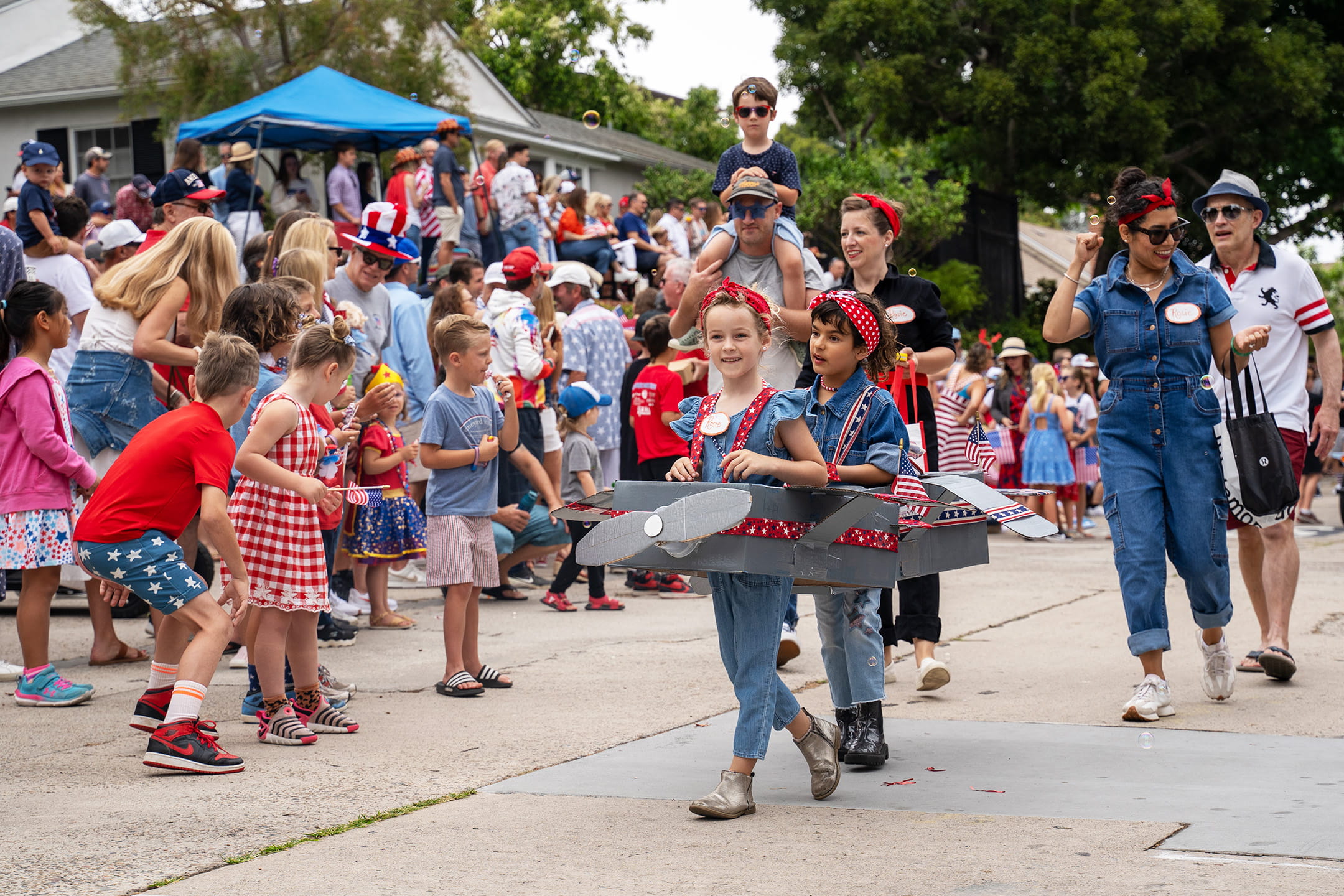Fourth of July in La Jolla parade, with children in patriotic Rosie the Riveter and vintage airplane costumes marching past a crowd of spectators.